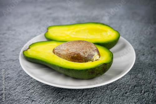Ripe avocado cut lengthwise into two pieces on white plate on gray table