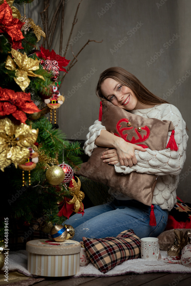 Young caucasian woman smiling next to a christmas tree hugging a christmas pillow Young caucasian woman smiling next to a christmas tree hugging a christmas pillow