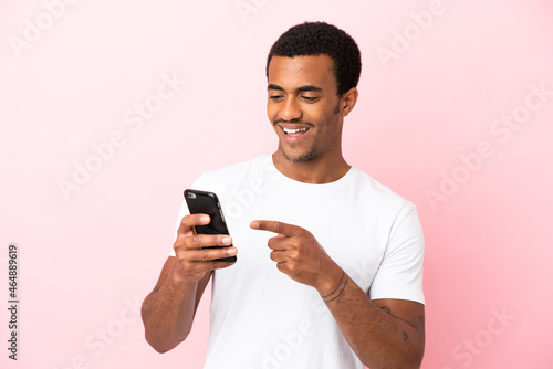 African American handsome man on isolated pink background sending a message or email with the mobile © luismolinero