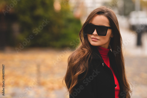 Outdoor autumn portrait of young elegant fashionable woman wearing trendy sunglasses and coat. Walking down the street of a European city