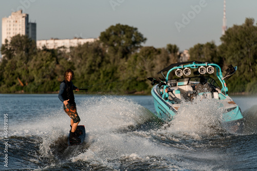 Bright motor boat pulls an active man riding a wakeboard and showing surfer gesture