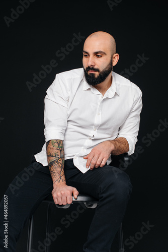 A young bearded man in a white shirt sits on a black background.