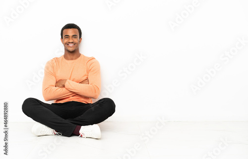 African American man sitting on the floor over isolated copyspace background with arms crossed and looking forward