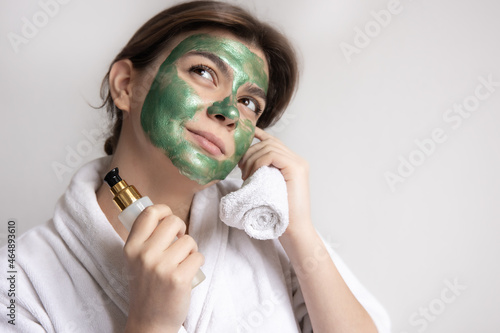 Cute young woman with green face mask and care products in hands, copy space. photo