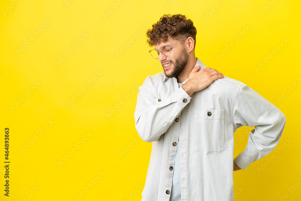 Young handsome caucasian man isolated on yellow background suffering from pain in shoulder for having made an effort Young handsome caucasian man isolated on yellow background suffering from pain in shoulder for having made an effort