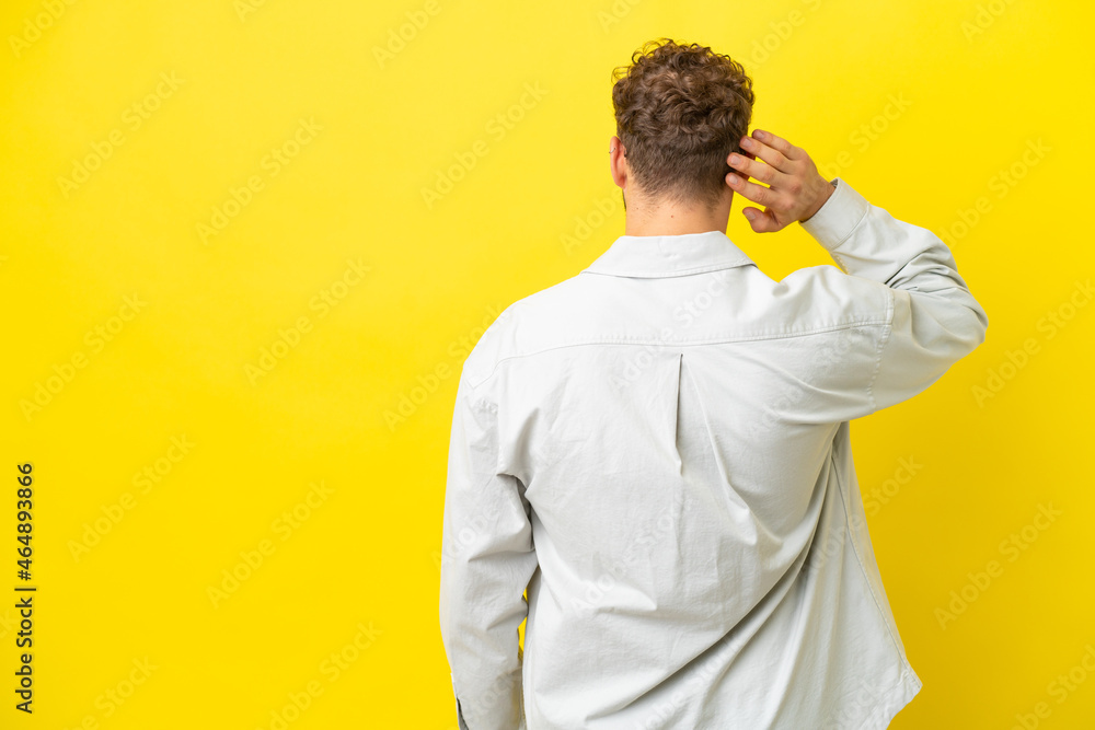 Young handsome caucasian man isolated on yellow background in back position and thinking Young handsome caucasian man isolated on yellow background in back position and thinking