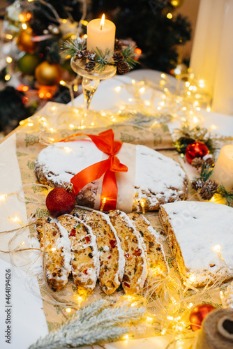 Fototapeta Naklejka Na Ścianę i Meble -  Traditional Christmas stollen made of dried fruits and nuts sprinkled with powdered sugar on the background of a Christmas decor with candles. Traditional Christmas cupcake.