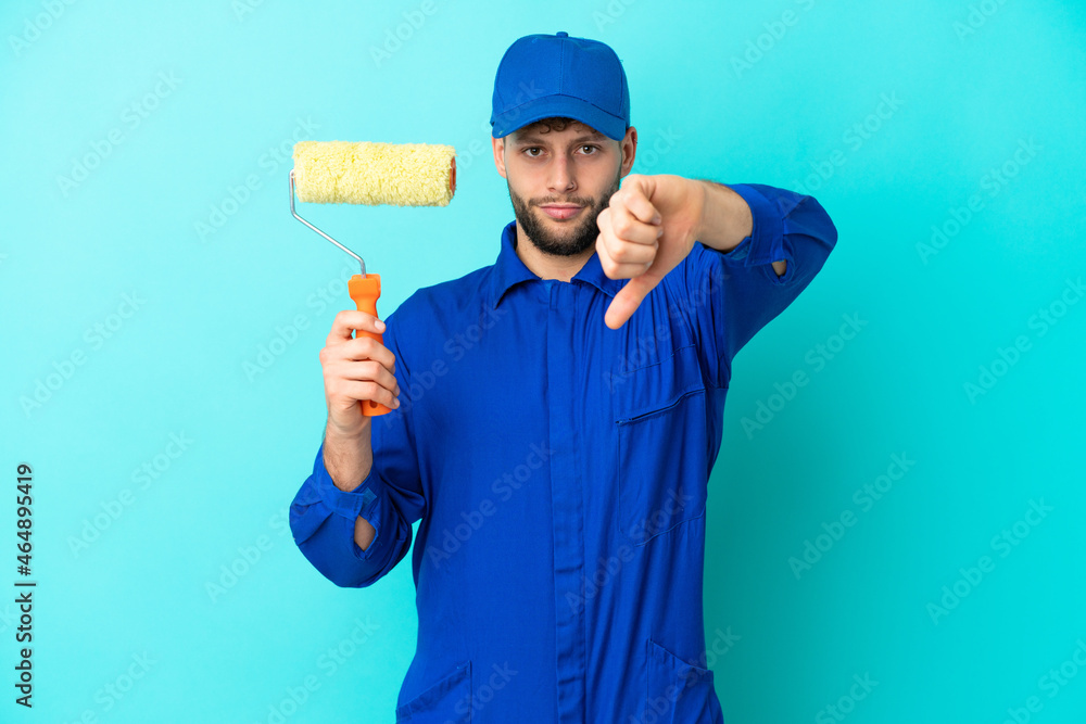 Painter caucasian man isolated on blue background showing thumb down with negative expression