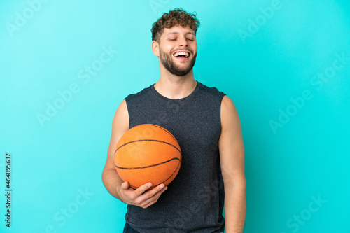Handsome young man playing basketball isolated on blue background laughing