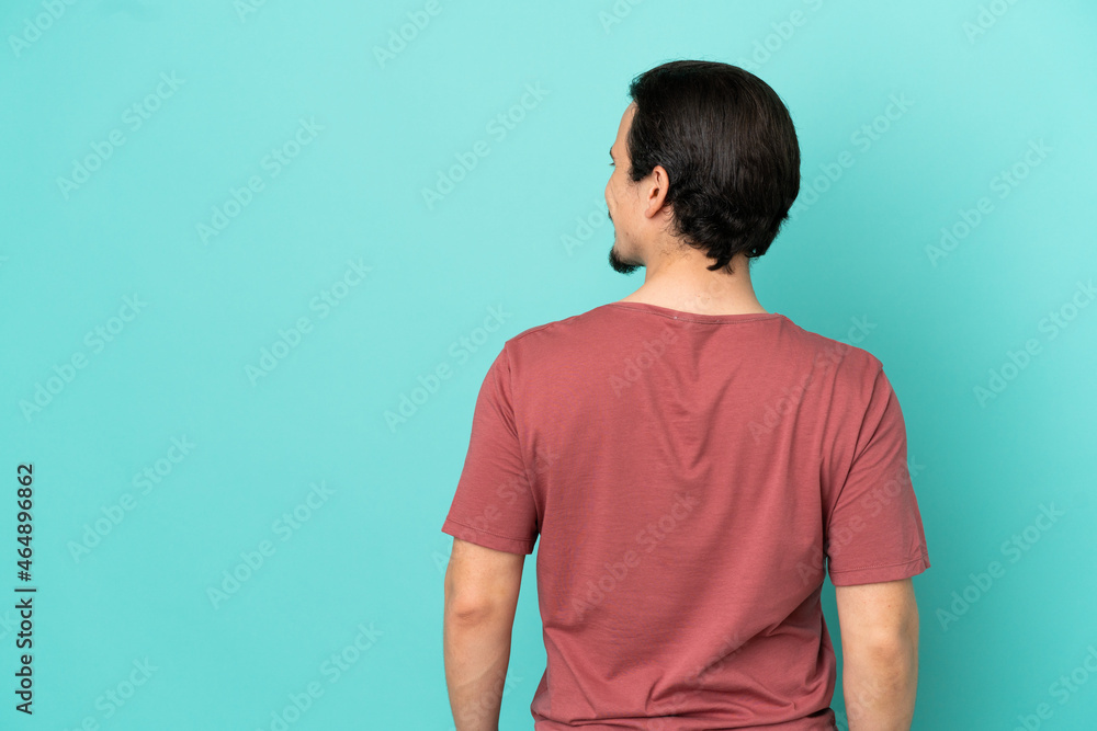 Young caucasian man isolated on blue background in back position and looking side Young caucasian man isolated on blue background in back position and looking side