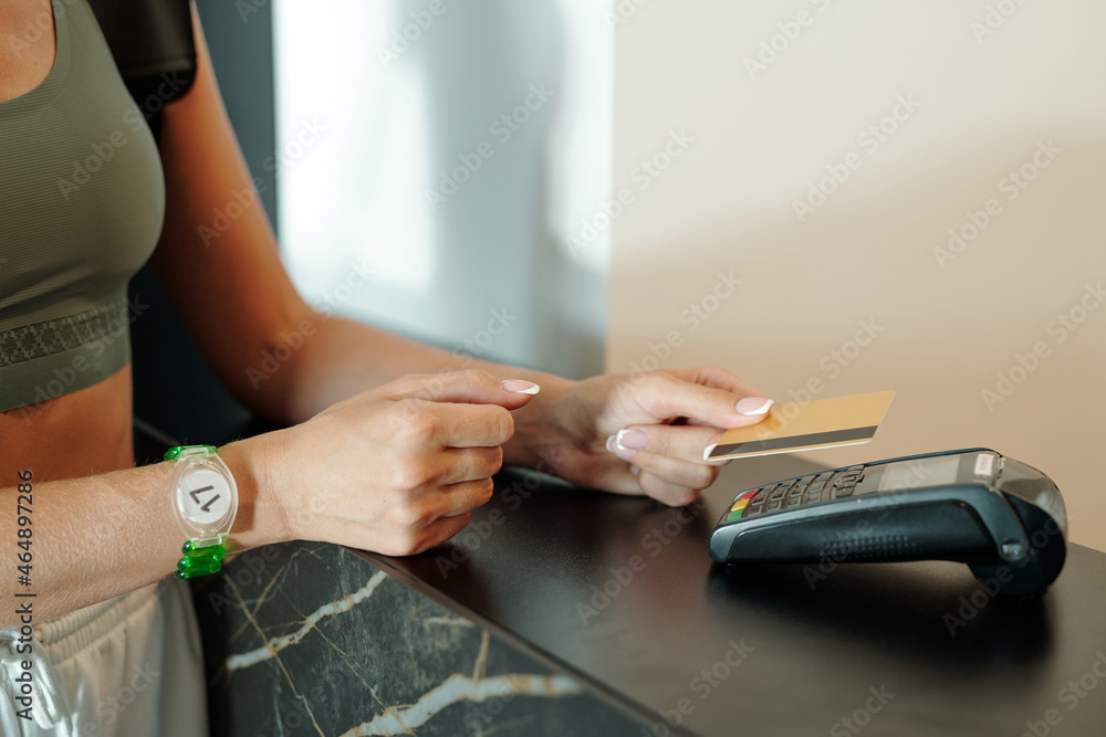 Obraz premium Hands of young woman holding credit card over payment terminal on reception counter in hotel or leisure center lounge