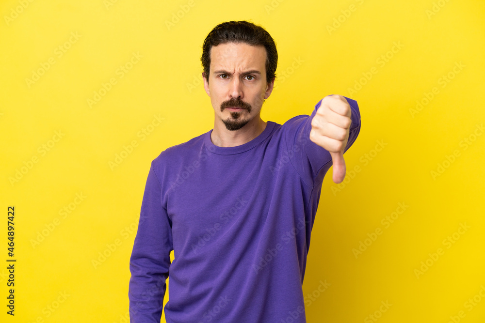 Young caucasian man isolated on yellow background showing thumb down with negative expression Young caucasian man isolated on yellow background showing thumb down with negative expression