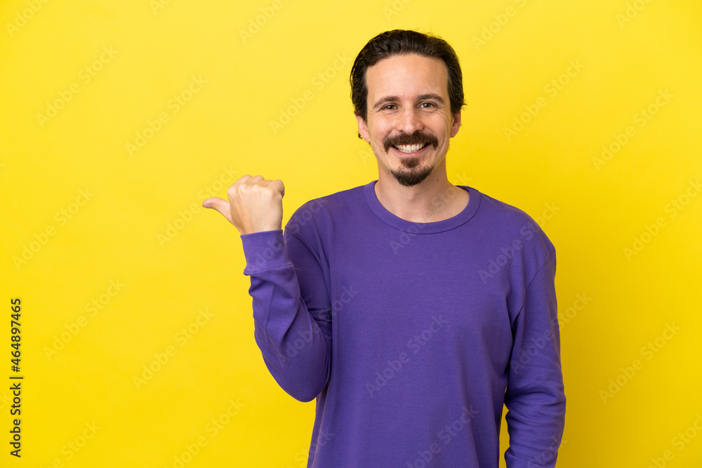 Young caucasian man isolated on yellow background pointing to the side to present a product Young caucasian man isolated on yellow background pointing to the side to present a product
