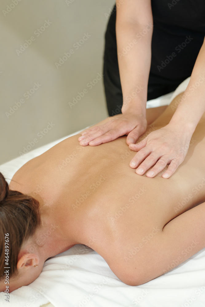 Fototapeta premium Hands of massage therapist touching back of young woman lying on white sheets in luxurious spa salon