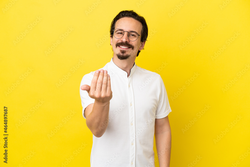 Young caucasian man isolated on yellow background inviting to come with hand. Happy that you came Young caucasian man isolated on yellow background inviting to come with hand. Happy that you came
