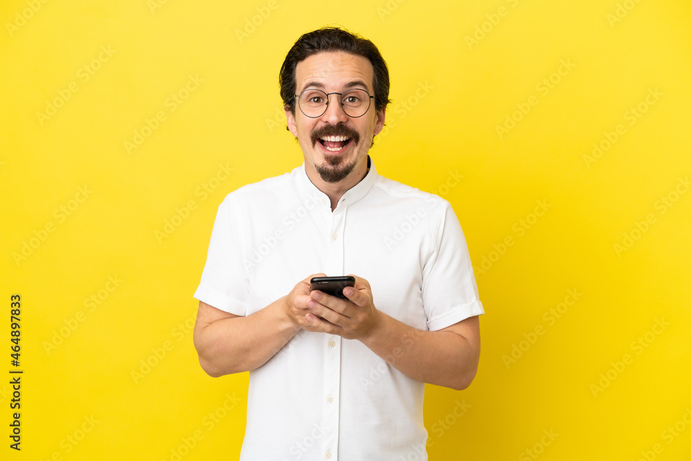 Young caucasian man isolated on yellow background surprised and sending a message Young caucasian man isolated on yellow background surprised and sending a message