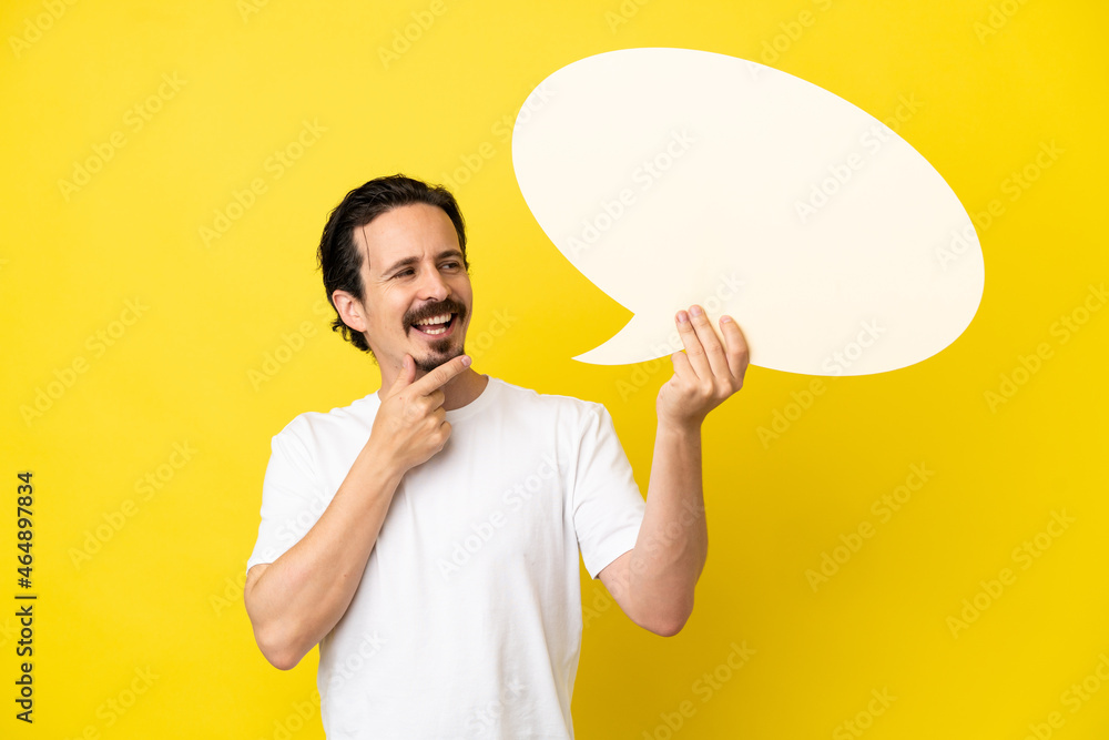 Young caucasian man isolated on yellow background holding an empty speech bubble and pointing it Young caucasian man isolated on yellow background holding an empty speech bubble and pointing it