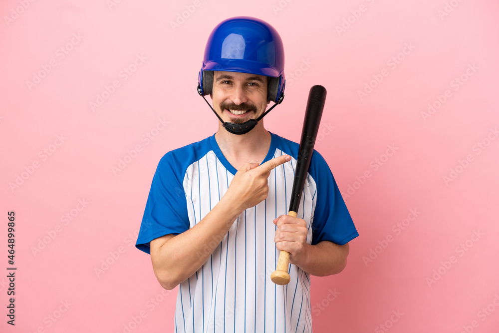 Young caucasian man playing baseball isolated on pink background pointing to the side to present a product