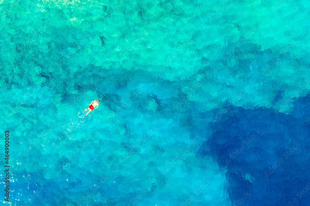 Aerial drone view of swimming man with red swimming trunks in turquoise water. Ionian sea, Kefalonia Island, Greece. Aerial drone view of swimming man with red swimming trunks in turquoise water. Ionian sea, Kefalonia Island, Greece.