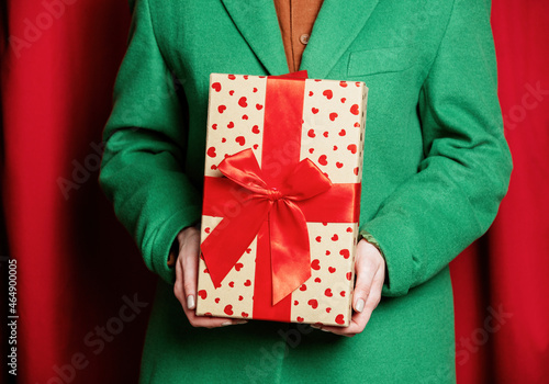 Woman in green jacket with holiday gift box on red curtains background