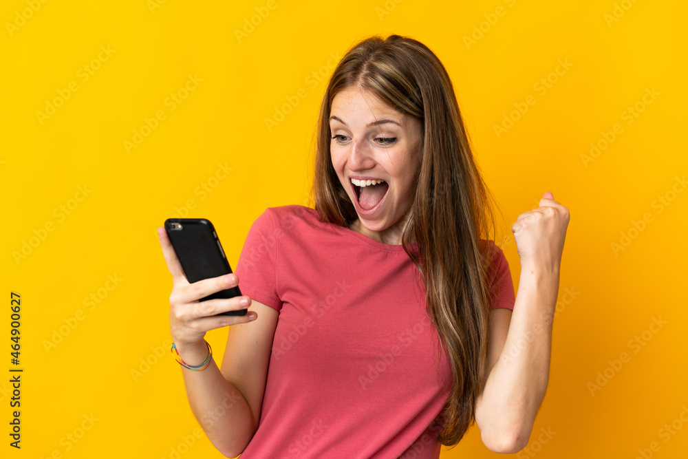 Young woman using mobile phone isolated on yellow background celebrating a victory Young woman using mobile phone isolated on yellow background celebrating a victory