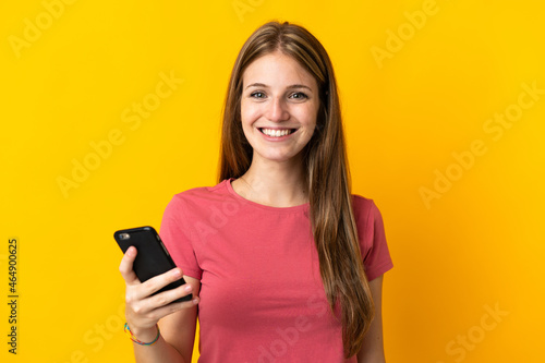 Young woman using mobile phone isolated on yellow background smiling a lot