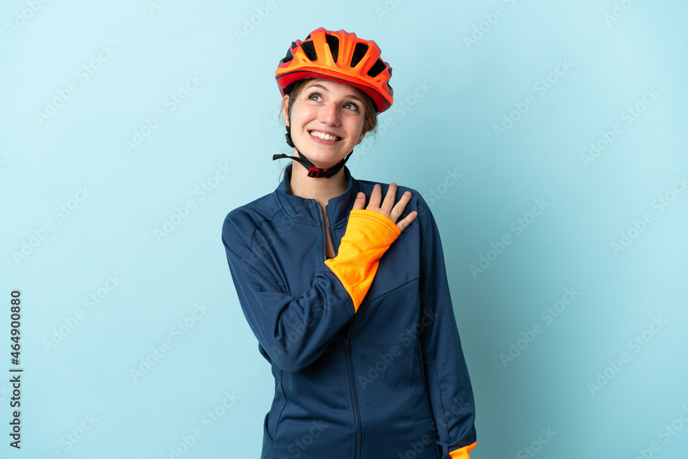 Young cyclist woman isolated on blue background looking up while smiling Young cyclist woman isolated on blue background looking up while smiling