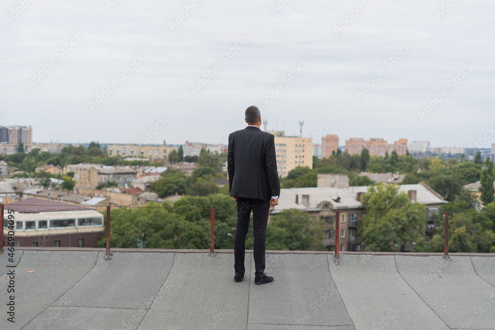 Businessman standing on a roof and looking at city Businessman standing on a roof and looking at city