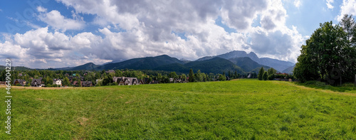 Panoramic view of green grass meadow countryside field with A shaped houses against sleeping knight tatra mountain aka as giewont and dramatic clouds located in Zakopane, South Poland, Europe