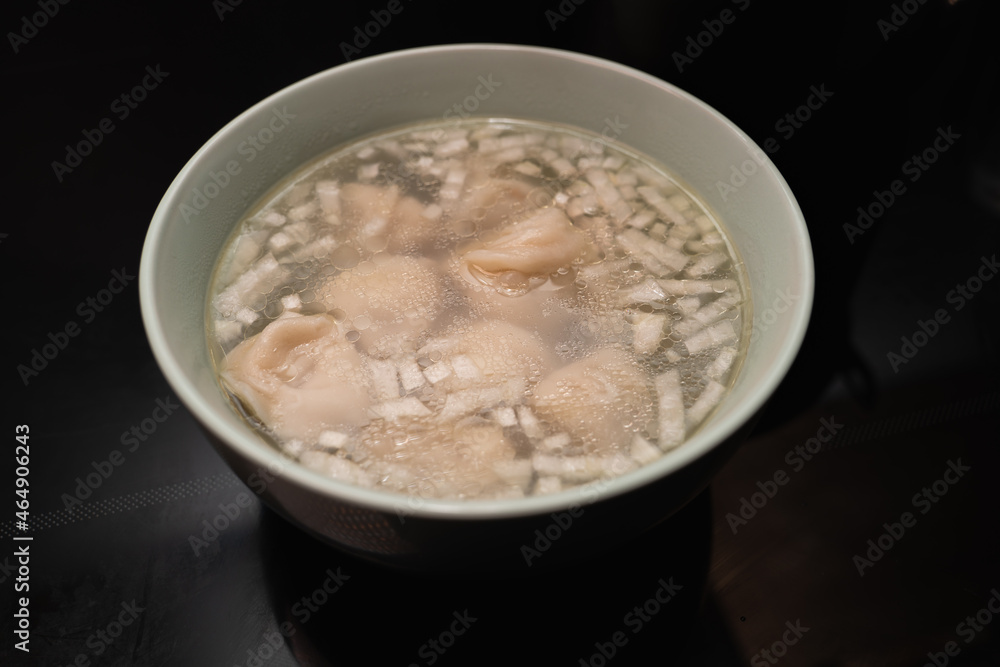 Dumplings with broth and onions in a plate on the black surface of an induction cooker Dumplings with broth and onions in a plate on the black surface of an induction cooker