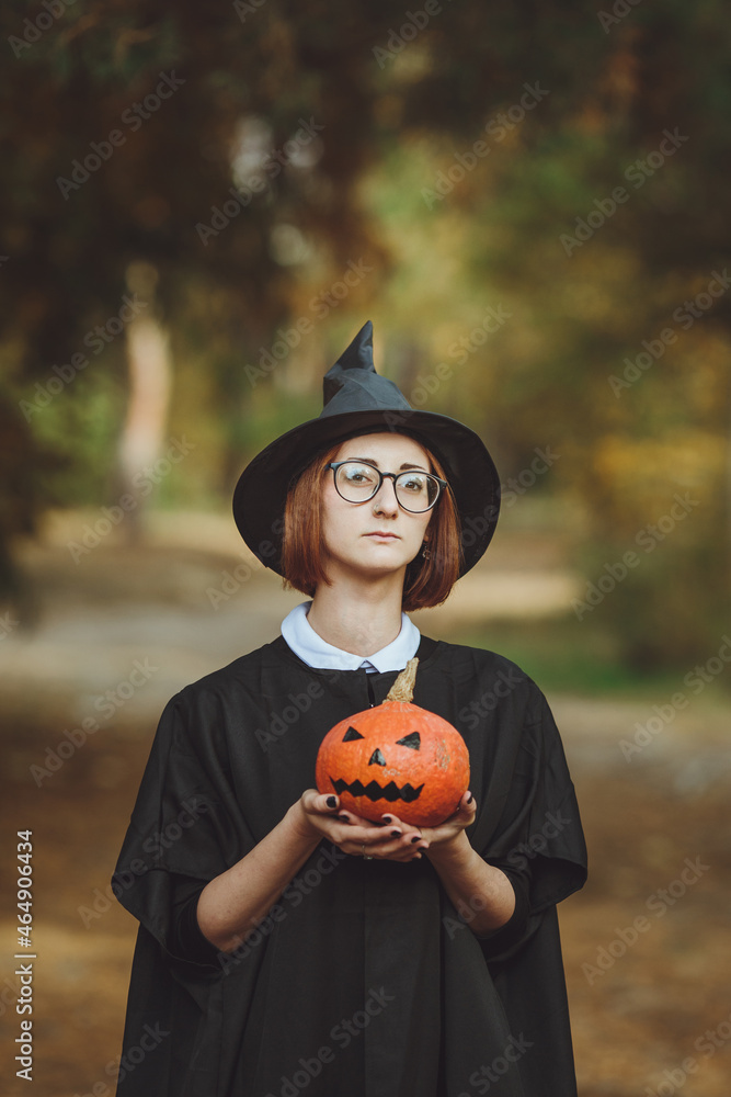 Halloween witch. Portrait of a girl in a hat and a witch costume with a pumpkin in the forest. Ready for the holiday