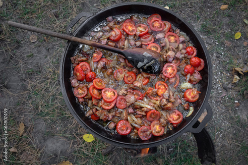 Tomatoes, onions and meat in a pan. Cook at a picnic. A traditional dish. Tomato slices. A fatty dish. Roast vegetables and bacon in a wok. A hearty dinner.
