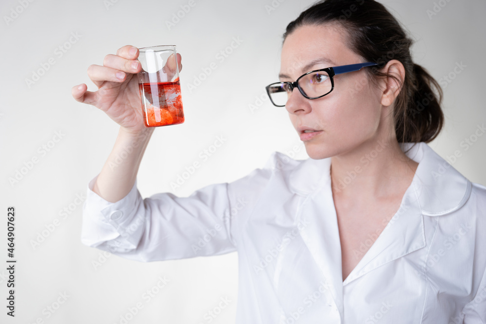 A doctor in a white coat uses a flask to study some red liquid, A doctor in a white coat uses a flask to study some red liquid,