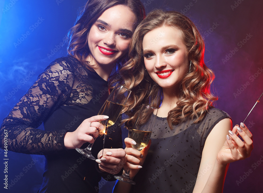Two beautiful young women in black dress with wine glasses and sparkle fire.