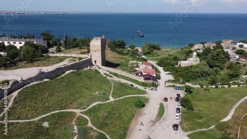 Scenic aerial view of the Tower of ancient ruined Genoese fortress Kaffa against blue sky and dark blue sea. Drone tracking shot, right to left.
