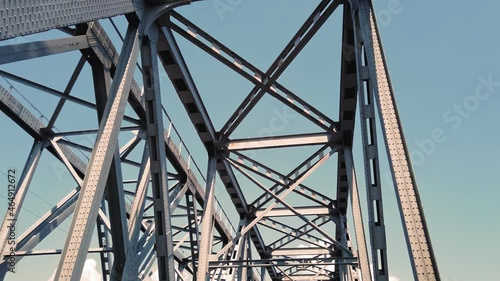 metal bridge. rough iron constructions against blue sky, filmed in motion from a car. bottom view. Railway and road bridge across the river. Silhouette of crossing steel beams. photo