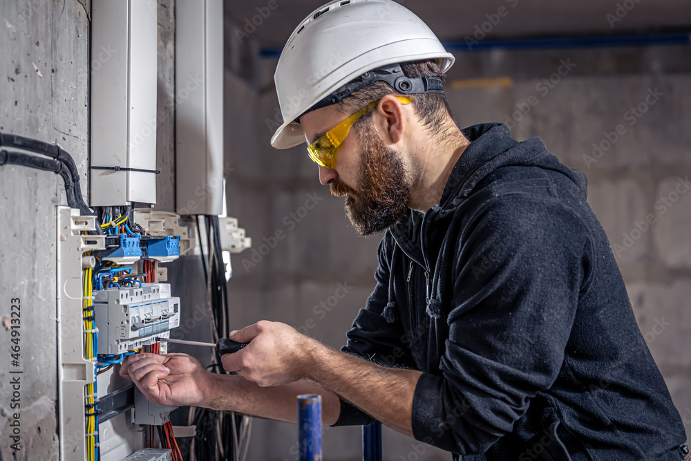 A male electrician works in a switchboard with an electrical connecting cable. A male electrician works in a switchboard with an electrical connecting cable.