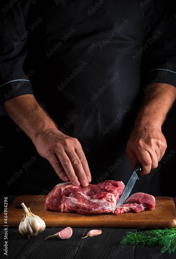 Professional chef cuts meat with a knife in kitchen prepares food. Vegetables and spices on the kitchen table in restaurant to prepare delicious lunch