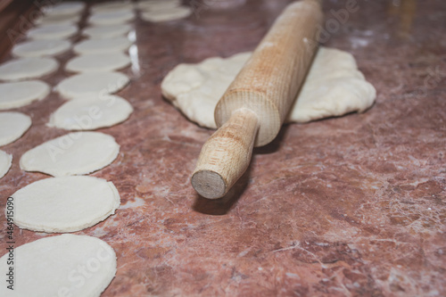 Dough under a wooden rolling pin on a marble kitchen countertop.