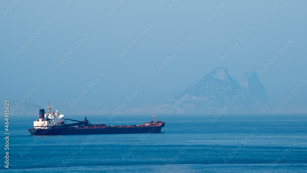 A freighter sails the Mediterranean Sea with the Rock of Gibraltar in the distance through the haze.