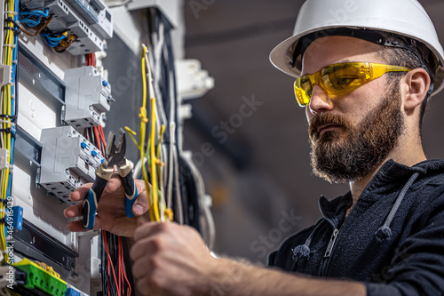 A male electrician works in a switchboard with an electrical connecting cable. photo