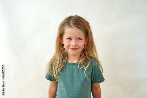 portrait of a happy child on a white background in a green t-shirt smiling. The little girl plays with her sly eyes. Happy girl. copy space. Childhood concept.