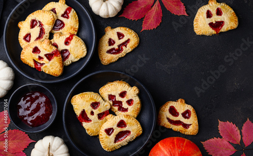 Mini halloween pumpkin hand pies with  strawberry jam. Jack-O-lantern cookies or pies on a black background. Halloween dessert. Top view. Copy space.