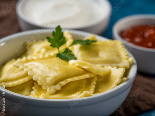 A portion of Italian ravioli with mint leaf, poured with melted butter and two sauces in the background. Macro photography. Restaurant, hotel, home cooking, café, cookbook.