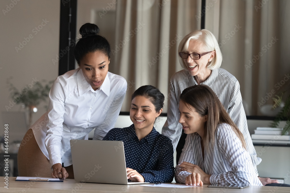 Smiling indian female show original project decision easy working solution on pc screen to multiethnic women colleagues of diverse age. Successful ethnic lady worker share new strategy with teammates