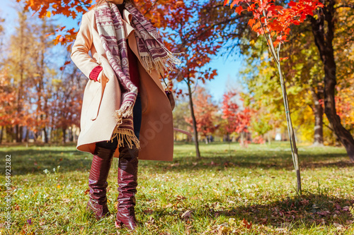 Stylish woman wearing warm clothes shoes and accessories walking in fall park. Autumn female outfit. Burgundy boots