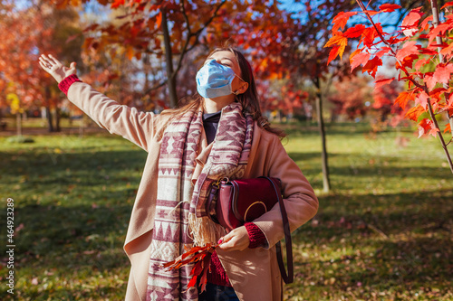 Young woman wears protective mask outdoors during coronavirus covid-19 pandemic in empty fall park.