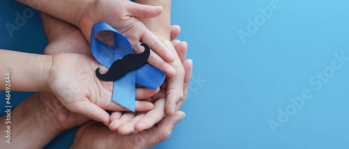 Family hands holding light blue ribbonwith mustache on blue background , Prostate Cancer Awareness, Men health awareness photo