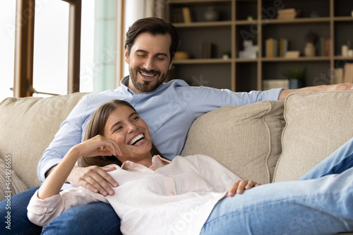 Принти на полотні Happy bonding loving laughing young 30s family couple relaxing on comfortable couch in modern living room, communicating talking speaking enjoying carefree leisure weekend time together at home
