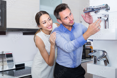 Young husband and wife are choosing new mixer tap in kitchen furnishing store.